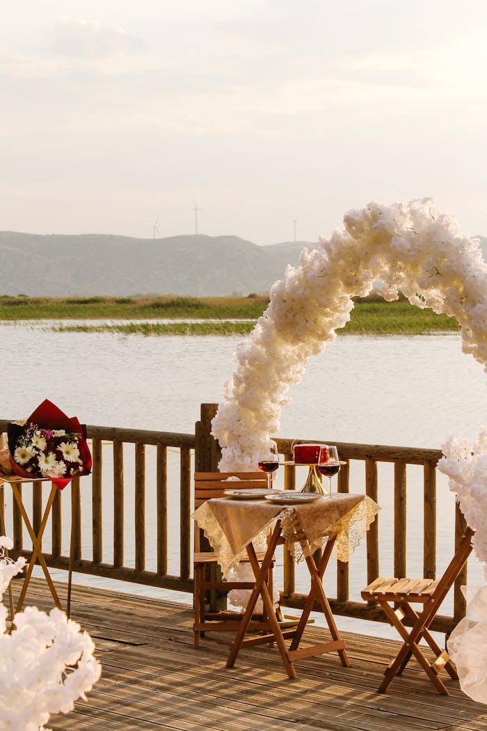 Elegant lakeside wedding table with white floral arch and wineglasses under a soft sunset light.
